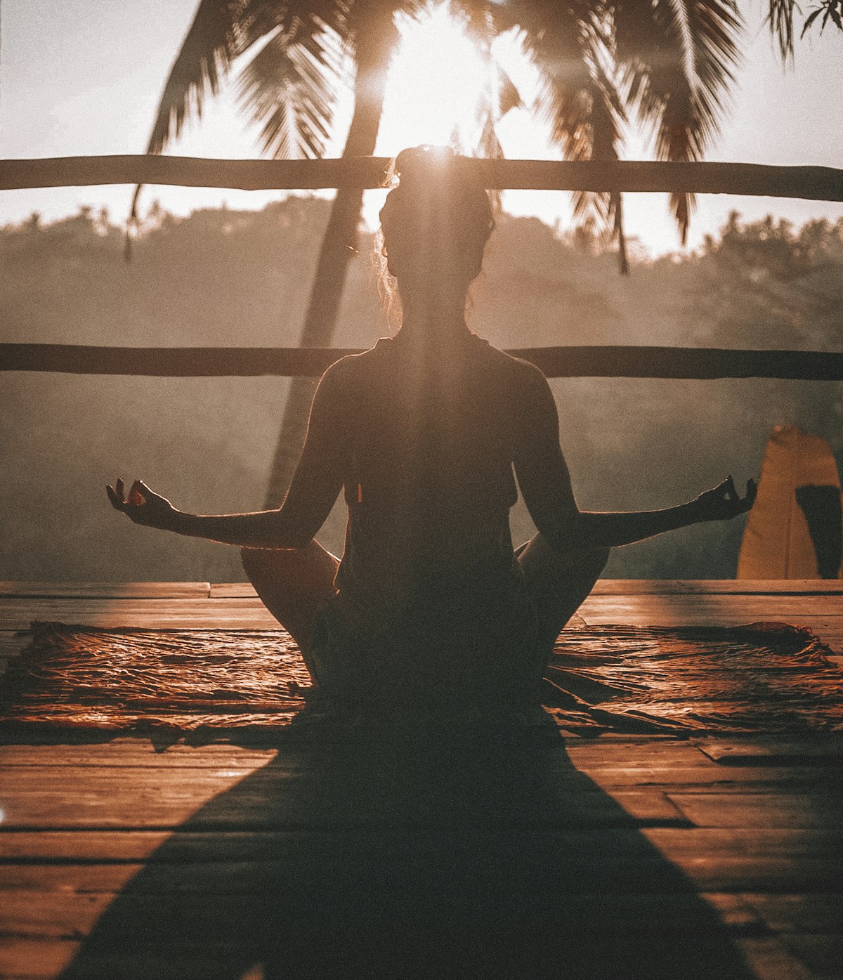 Person meditating on a beach deck at sunrise